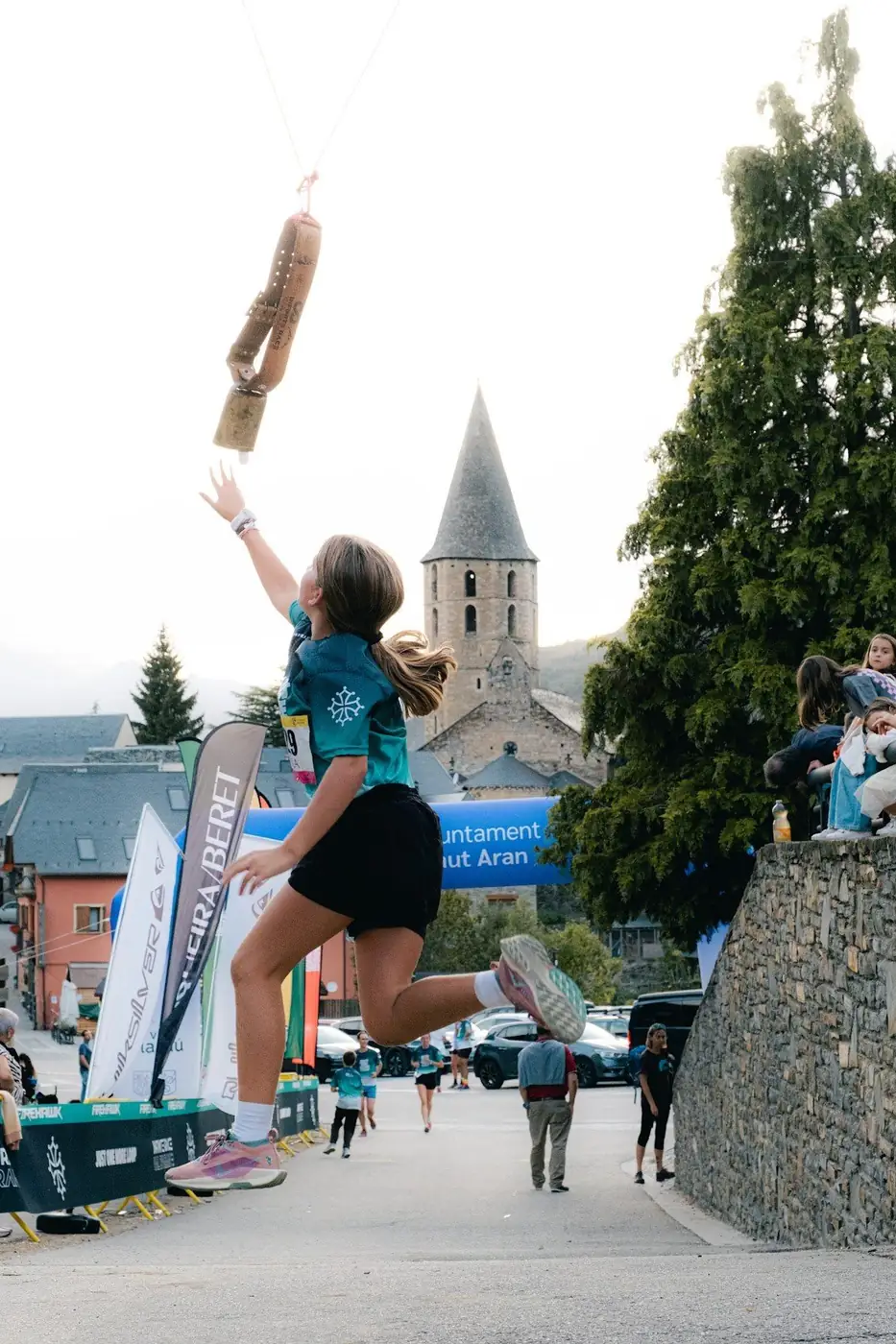 Una niña salta para tocar el jamón de la meta, con la iglesia de Salardú detrás